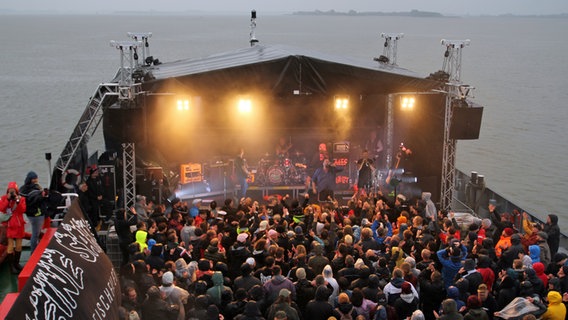 Eine Band spielt auf einer Bühne auf einem Schiff, davor Menschen in Regenkleidung © NDR / Marian Schäfer Foto: Marian Schäfer