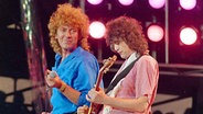 Led Zeppelin-Sänger Robert Plant (links) und -Gitarrist Jimmy Page bei einem Auftritt auf einem Live Aid Konzert in Philadelphia im Juli 1985 auf der Bühne. Page spielt Gitarre, während ihn Sänger Plant anschaut und lächelt. © picture alliance / AP Photo | AMY SANCETTA Foto: picture alliance / AP Photo | AMY SANCETTA