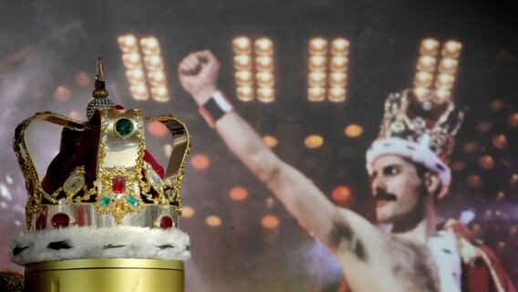 Eine Krone und dahinter ein Bild von einem Rockstar auf der Bühne, der die Krone trägt. © Kirsty Wigglesworth/AP/dpa Foto: Kirsty Wigglesworth
