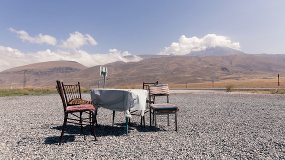 Einzelne Stühle stehen um einen Tisch an einer Straße am Berg Ararat © NDR.de/Christina Grob Foto: Christina Grob