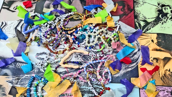 Viele Armbänder mit bunten Perlen, weißen Steinen und Buchstaben mit Wörtern © NDR Foto: Patricia Batlle