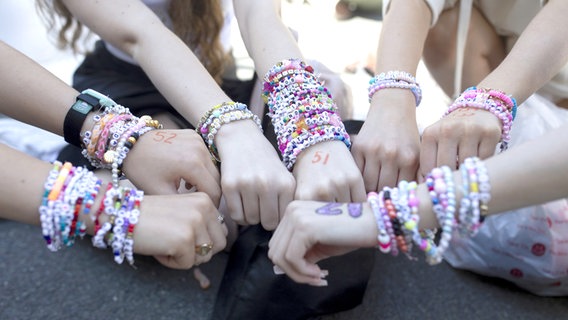 Mehrere Arme nebeneinander voller Armbänder - Bracelets -  von "Swifties", also Taylor-Swift-Fans mit bunten Perlen, weißen Steinen und Buchstaben mit Wörtern © PA Wire/dpa Foto: Charlotte Coney