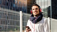 Junger bärtiger Mann mit Kopfhörern und Smartphone in der Hand an einem sonnigen Tag © photocase.de Foto: raferto
