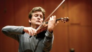 Ein Mann spielt Geige, dahinter spielt ein Orchester - Geiger Christian Tetzlaff bei einem Auftritt in München © Imago Stock & People Foto:  MichelxNeumeister