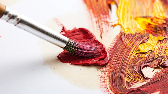 Ein Pinsel mit roter Farbe rührt in weiteren Farben (gelb, orange), die sich mischen.
Rote, schwach beleuchtete Stuhlreihen vor einer beleuchteten Kinoleinwand © Fotolia 