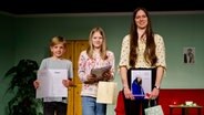 Die drei Gewinner des Vorlesewettbewerbs "Schölers leest Platt" stehen mit ihren Siegerurkunden auf der Bühne. © NDR Foto: Lornz Lorenzen