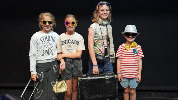 Vier Kinder stehen auf einer Bühne und freuen sich auf die Premiere ihres selbstgeschriebenen Stücks. © NDR Foto: Lornz Lorenzen