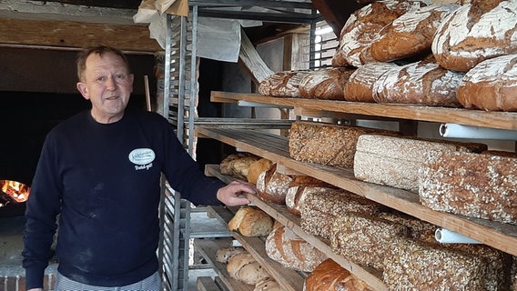 Bäcker Jürgen Küpnick steht neben Regalen voller Backwaren. © NDR Foto: Alexa Dudda