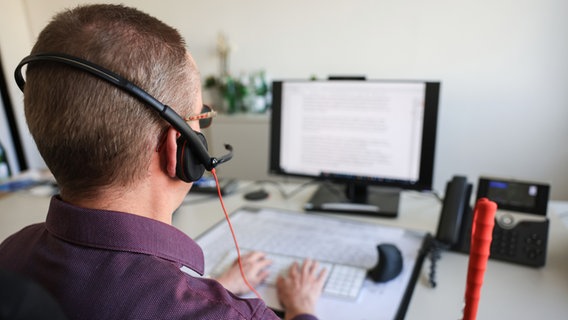 Ein sehbehinderter Mitarbeiter mit Headset auf dem Kopf sitzt in seinem Büro am Bildschirmarbeitsplatz. © picture alliance/dpa | Oliver Berg 