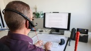 Ein sehbehinderter Mitarbeiter mit Headset auf dem Kopf sitzt in seinem Büro am Bildschirmarbeitsplatz. © picture alliance/dpa | Oliver Berg 