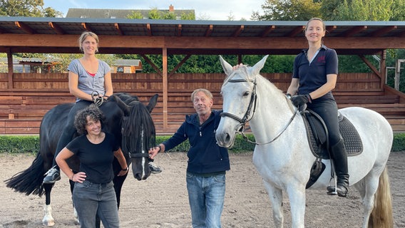 Drei Frauen und ein Mann posieren mit zwei Pferden vor einer Tribüne aus Holz. © NDR Foto: Paula-Neele Deusing