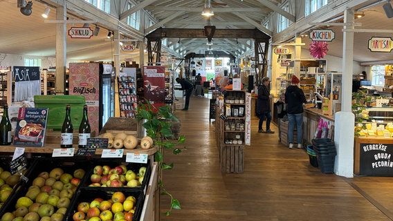 Der Biomarkt von innen. Im Vordergrund sieht man Obst und Gemüse. Rechts sieht man die Käsetheke. In der Mitte blickt man in Fluchtperspektive auf die Länge des Ladens und die Bühne am Ende der Halle. © NDR Kultur Foto: Tom Holste, Cornelius Kob