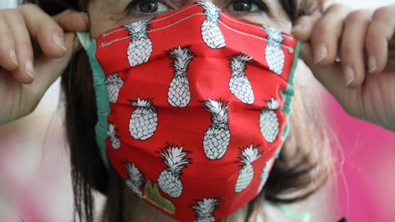 Eine Frau setzt sich eine selbstgemachte Schutzmaske auf. © picture alliance/Oliver Berg/dpa Foto: Oliver Berg