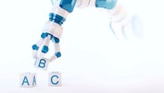Ein Roboterarm legt Buchstaben-Würfel nebeneinander © imago 