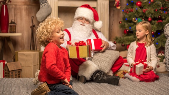 happy santa claus und kinder sitzen auf dem teppich mit weihnachtsgeschenken © picture alliance Foto: PantherMedia | LightField Studios