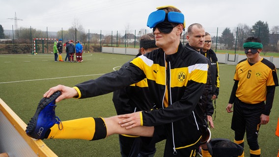 Fußballspieler mit verbunden Augen dehnt sein linkes Bein am Spielfeldrand. © NDR Foto: Rainer Schildberger