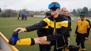 Fußballspieler mit verbunden Augen dehnt sein linkes Bein am Spielfeldrand. © NDR Foto: Rainer Schildberger