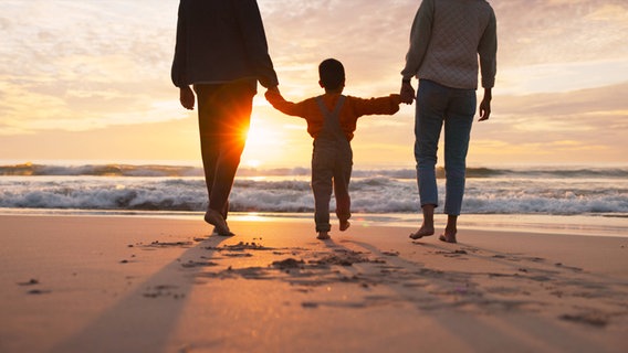 Eine Familie läuft am Strand entlang. © IMAGO/Zoonar II Foto: Zoonar II