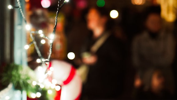 Eine Nahaufnahme von Weihnachtslichtern auf einem Markt mit einem unscharfen Hintergrund mit Menschen. © IMAGO / Wirestock 