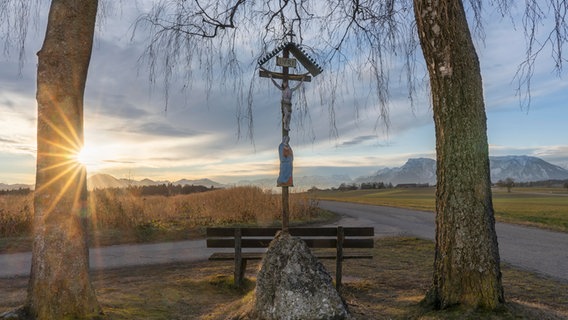 Ein Sonnenaufgang - im Vordergrund ein Wegkreuz. © picture alliance / Shotshop | ROHA-Fotothek Fürmann Foto: ROHA-Fotothek Fürmann