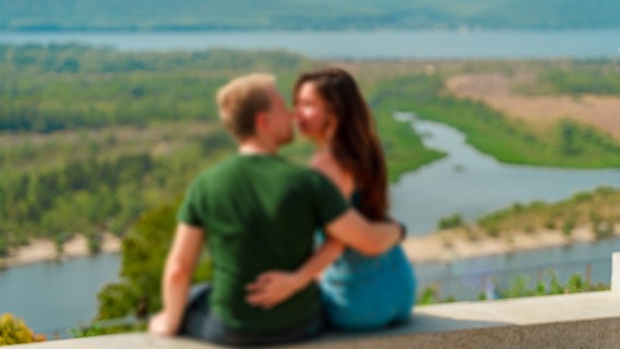 Ein unscharfes Foto mit einem Mann und einer Frau, die sich umarmen und vor einem Panorama der Wolga sitzen. © IMAGO / Dreamstime 