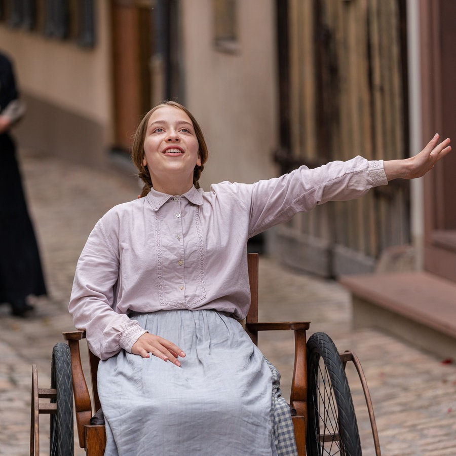 Ein Mädchen sitzt im Rollstuhl und hebt den Arm. © LOOKSfilm 