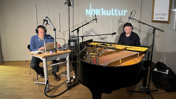 Links sitzt Roman Flügel vor seinem Laptop und rechts daneben sitzt Florian Weber an einem schwarzen Flügel, beide haben Kopfhörer auf. © NDR Foto: Claus Röck