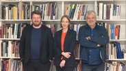 Alexander Solloch, Sibylle Anderl und Raoul Schrott stehen lächelnd nebeneinander vor einer Bücherwand. © NDR Foto: Meike Egge