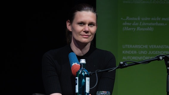 Kerstin Preiwuß sitzt auf einer Bühne vor einem Mikrofon und blickt in die Kamera. © Reiner Mnich Foto: Reiner Mnich