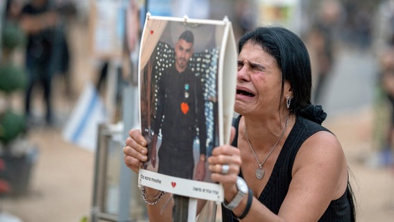 Eine weinende Frau hält ein Plakat hoch, auf dem ein junger Mann abgedruckt ist. © dpa Foto: Ilia yefimovich