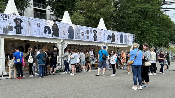 Viele Menschen stehen vor einem Merchandise Stand für Taylor Swift Klamotten. © Julia Hercka / NDR Foto: Julia Hercka / NDR