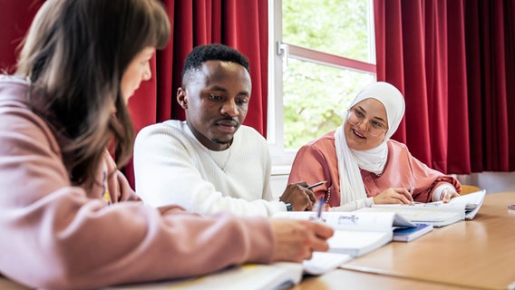 Drei Erwachsene sitzen an Schultischen und hören einander zu © Gesche Jäger/Volkshochschule Hamburg Foto: Gesche Jäger