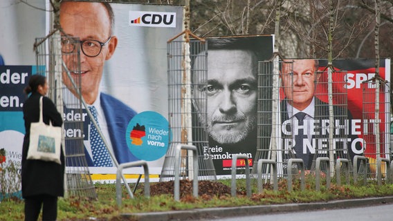 Eine Frau steht vor mehreren Wahlplakaten © IMAGO / dts Nachrichtenagentur 