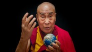 Der Dalai Lama hält einen kleinen Globus in der Hand und blickt in die Kamera. © picture alliance/dpa/X Verleih AG | - 