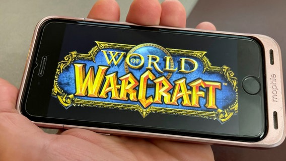 Eine Hand hält ein Smartphone, auf der das Logo vom Computerspiel "World of Warcraft" zu sehen ist. © picture alliance / STRF/STAR MAX/IPx 