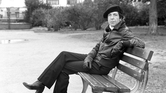 Der kanadische Musiker Leonard Cohen sitzt im Jahr 1976 mit einer Mütze auf einer Bank in Frankfurt am Main. © picture alliance / dpa | Istvan Bajzat Foto: picture alliance / dpa | Istvan Bajzat