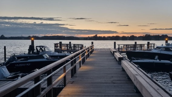 Ein Bootssteg. Links und rechts liegen Boote im Wasser. Am Horizont das  Ufer der Schlei im Abendrot. © NDR Foto: Bettina Seewald