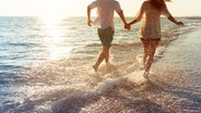 Junges Paar läuft bei Sonnenuntergang fröhlich am Meer. © fotolia Foto: fotofabrika
