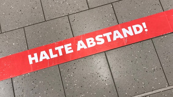 Auf dem Boden klebt ein Streifen mit der Aufschrift " Halte Abstand" © imago-images Foto: Waldmüller