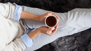 Eine Frau sitzt mit einem Kaffee auf dem Sofa. © s_karau / photocase.de Foto: s_karau / photocase.de