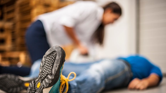 Eine Frau leistet einem bewusstlosen Mann, der auf dem Boden liegt, Erste Hilfe. © pixelaway / photocase.de Foto: pixelaway / photocase.de