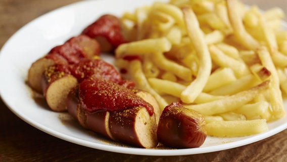 Auf dem Bild ist ein Teller mit einer Currywurst und Pommes zu sehen. © imago/Westend61 