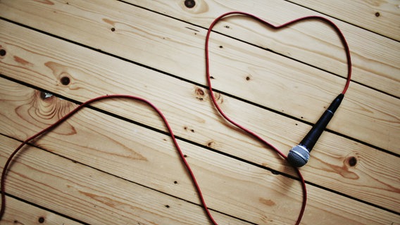 Ein Mikrofon liegt auf einem Holzboden und das Kabel formt ein Herz. © mathesch / photocase.de Foto: mathesch / photocase.de