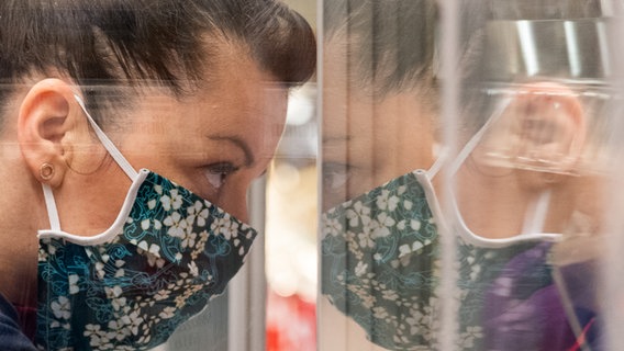 Eine Frau trägt einen bunten Mundschutz und lehnt gegen ein Fenster. © picture alliance/Robert Michael/dpa-Zentralbild/dpa Foto: Robert Michael