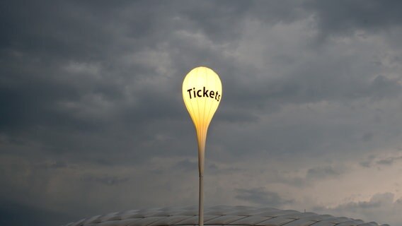 Über einem Stadion hängt ein leuchtender Luftballon mit dem Wort "Tickets". © picture alliance / dpa Foto: Sven Hoppe