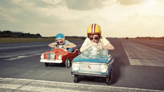 Zwei Jungs mit Helmen fahren in kleinen Autos ein Rennen. © imago/Westend61 Foto: Westend61