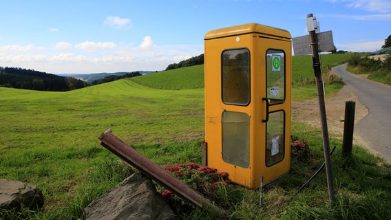 Eine gelbe Telefonzelle steht an einer Landstraße zwischen grünen Feldern. © imago/Manngold 