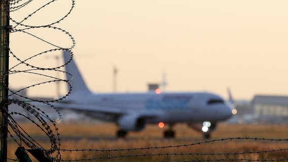 Symbolfoto zum Thema Abschiebung, Abschiebefluege (Abschiebeflüge), ein Flugzeug startet auf dem Flughafen Frankfurt a.M., im Vordergrund ein Sicherheitszaun mit Stacheldraht © picture alliance / Rene Traut Fotografie | Rene Traut Foto: Rene Traut Fotografie