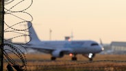 Symbolfoto zum Thema Abschiebung, Abschiebefluege (Abschiebeflüge), ein Flugzeug startet auf dem Flughafen Frankfurt a.M., im Vordergrund ein Sicherheitszaun mit Stacheldraht © picture alliance / Rene Traut Fotografie | Rene Traut 