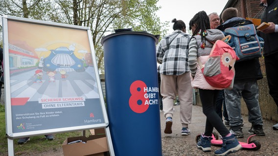 Zum Auftakt der dreiwöchigen Verkehrssicherheitsaktion stehen Schüler und ihre Eltern am Eingang der Grundschule Charlottenburger Straße "Rücksichtnahme auf Kinder...ist wichtig!" informierte die Hamburger Polizei. © picture Alliance / dpa Foto: Christian Charisius